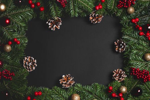Christmas Border frame of tree branches and red berries on black paper background flat lay top view mock-up