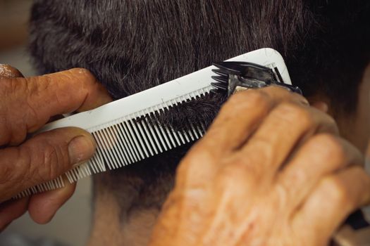 Closeup hand of hairdresser cutting hair with clipper at local barber shop.