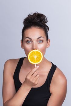 Portrait of beautiful woman with perfect skin holding orange slice on stick