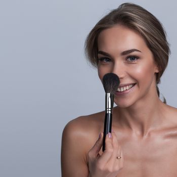 Portrait of beautiful woman smiling holding makeup brush on gray background
