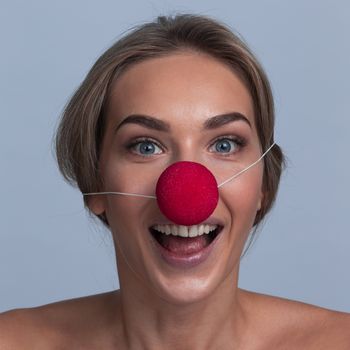 Happy young girl with red clown nose over gray background