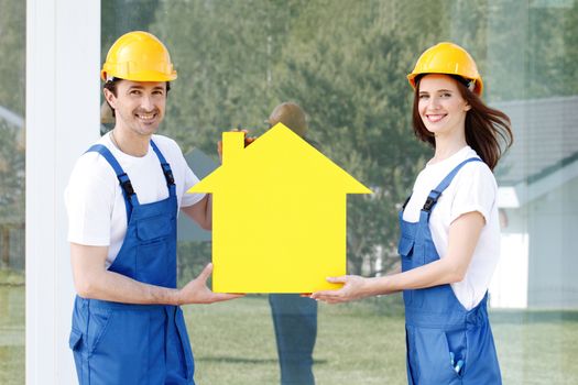 Two happy smiling workers hold yellow house model outdoors at construction site