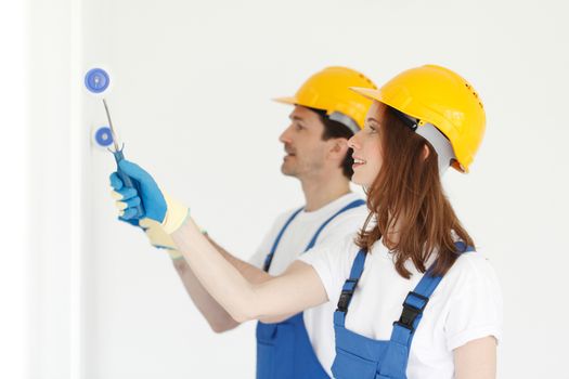 Happy young couple in uniform painting walls in their new house. Repair, construction and mortgage concept.