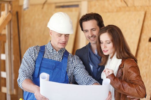 Foreman shows house design plans to a young couple at construction site