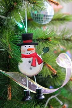 Toy funny iron snowman hanging on Christmas tree. New Year, holiday background with place for text. Pine decorated with ribbons and garlands. Front view. Vertical.