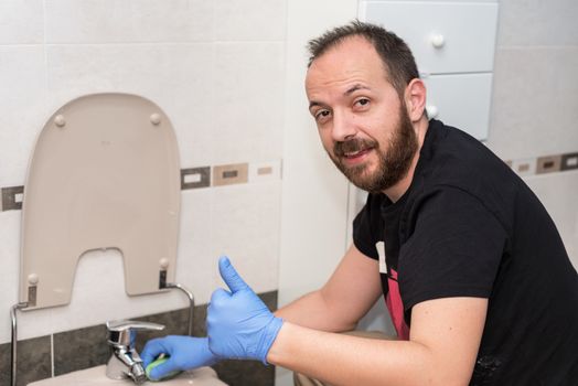 Man cleaning toilet bowl. Positive emotion showing thumbs up.