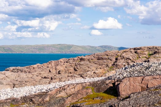 Behind a large rocky, wind-speckled hillock you can see the azure Barents sea, the Arctic ocean. Beautiful places near Teriberka, Murmansk region