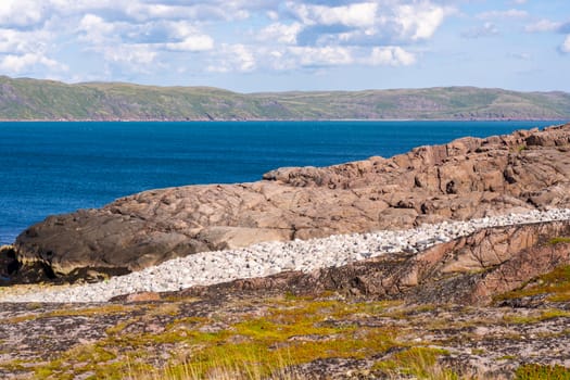 The stone shore separates the viewer from the delightfully bright cool Barents sea. In the background, ancient mountains seem to grow out of the water