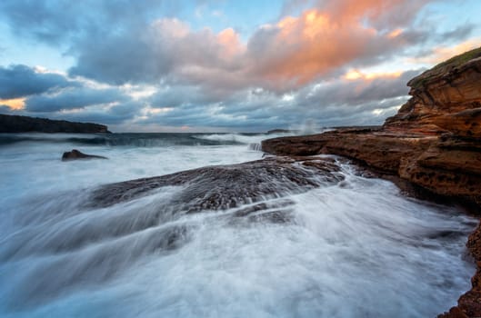 Large waves  crash onto the rocky shore and another large wave follows behind at Bare Island near Sydney Australia