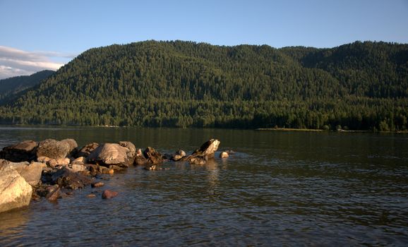 A ridge of stones running from the shore to a mountain lake at sunset. Teletskoye Lake, Altai, Russia.