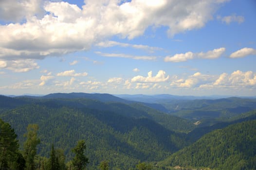 The tops of the mountains under white cumulus clouds from a bird's eye view. Altai, Siberia, Russia.