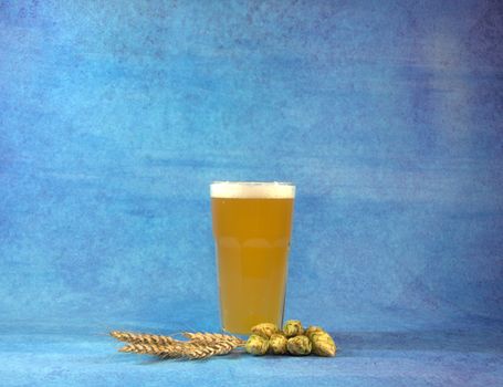 Glass of wheat beer with hops and sprinkles on a blue abstract background. Close-up.