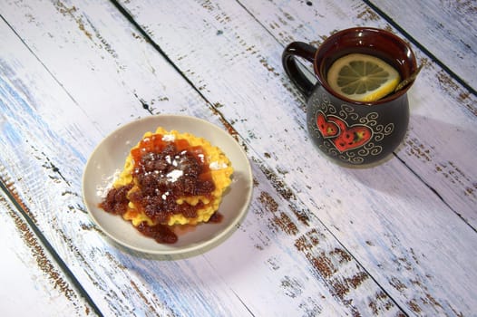 A mug of tea with lemon and a plate of waffles with strawberry jam. Close-up.