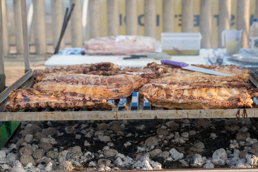 BBQ rack of pork ribs lined up on a large outdoor grill with smoke coming up from the fire below.