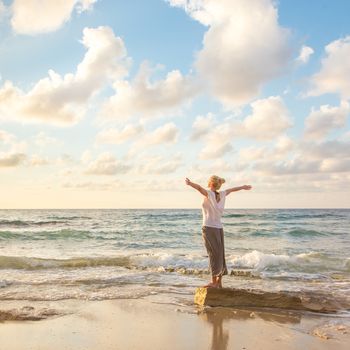 Relaxed woman enjoying sun, freedom and life an beautiful beach in sunset. Young lady feeling free, relaxed and happy. Concept of vacations, freedom, happiness, enjoyment and well being.