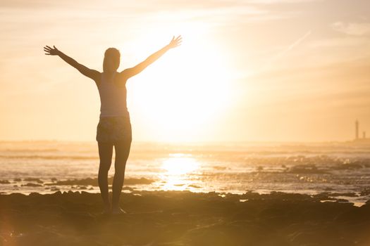 Silhouette of free woman enjoying freedom feeling happy at beach at sunset. Serene relaxing woman in pure happiness and elated enjoyment with arms raised outstretched up.