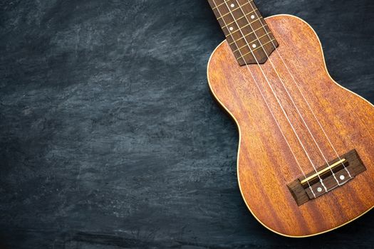 Ukulele on black cement background. Body and bridge of ukulele parts. Copy space for text. Concept of summer ukulele or Hawaiian musical instruments.