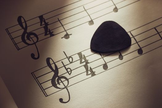 Music notes and black guitar pick  in morning light. Closeup and copy space for text. Concept of Music lovers.