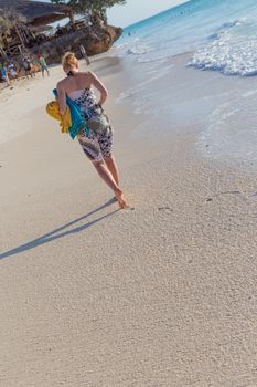 Happy woman enjoying in summer, walking joyfully on tropical beach. Beautiful caucasian model on vacations on sandy beach. Footprints in sand.