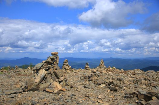 A small cairn on top of a mountain overlooking hilltops under the clouds. Altai, Siberia, Russia.