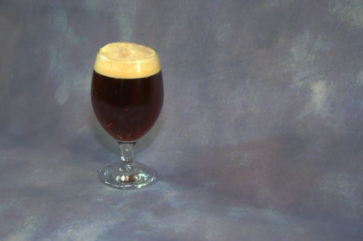 Glass of dark beer with foam on a gray abstract background. Close-up.