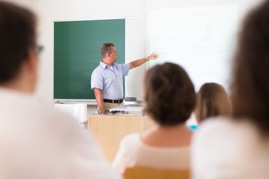 Teacher at university in front of a whiteboard screen. Students listening to lecture and making notes.