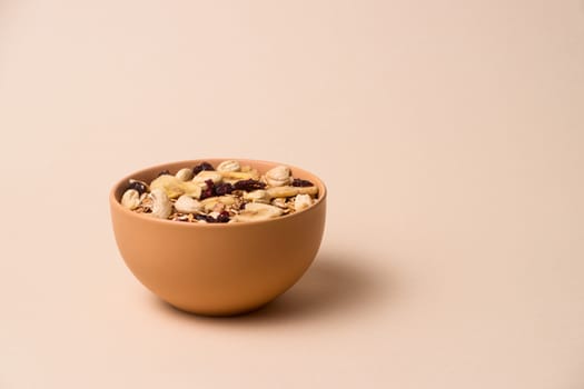 A fresh granola with dried and candied nuts and fruits in beige colour bowl closeup on beige bakground. Concept of nutrient and healty breakfast or meal