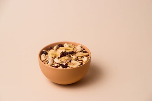 A fresh granola with dried and candied nuts and fruits in beige colour bowl closeup on beige bakground. Concept of nutrient and healty breakfast or meal