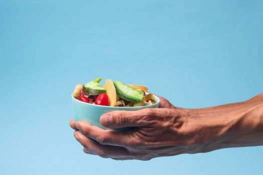 Male hands holding a full blue bowl of candied fruits and nuts on blue background. Stock photo of nutrient and healty food. Conceptual photo of vegan and vegetarial food and meal.