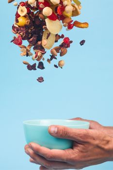 Male hands holding an empty blue bowl on blue background. Candied fruits and nuts flying above the bowl. Stock photo of nutrient and healty food. Conceptual photo of vegan and vegetarial food and meal.