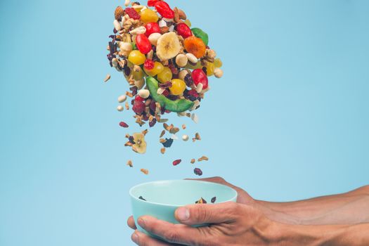 Male hands holding an empty blue bowl on blue background. Candied fruits and nuts flying above the bowl. Stock photo of nutrient and healty food. Conceptual photo of vegan and vegetarial food and meal.