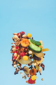 Dried and candied fruits and nuts flying on blue background. Stock photo of healty and nutrient food. Conceptual photo of vegan and vegetarian healty food.