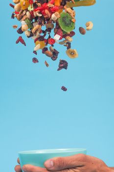 Male hands holding an empty blue bowl on blue background. Candied fruits and nuts flying above the bowl. Stock photo of nutrient and healty food. Conceptual photo of vegan and vegetarial food and meal.