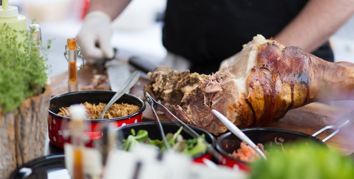 Cheff preparing traditional dish with cuts of pork ham meat on street stall on international street food festival of Odprta kuhna, Open kitchen event, in Ljubljana, Slovenia.