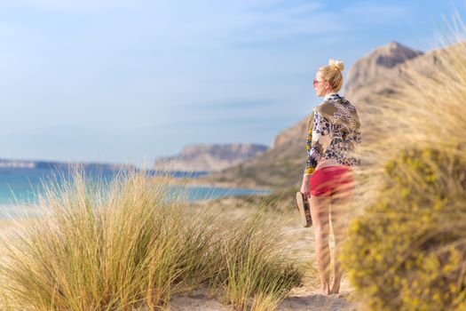 Relaxed woman wrapped in colorful scarf, enjoying sun, freedom and life at beautiful Balos beach in Greece. Concept of holidays, vacations, freedom, joy and well being.