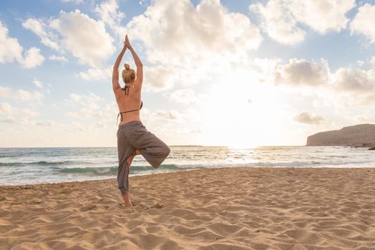 Active young woman practicing yoga on beach at sunset.