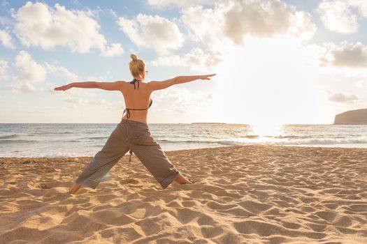 Active young woman practicing yoga on beach at sunset.