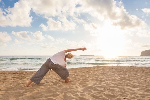 Active young woman practicing yoga on beach at sunset.