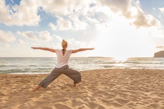 Active young woman practicing yoga on beach at sunset.