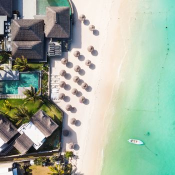 Aerial view of beautiful tropical beach front hotel resort with swimming pool, palm leaves umbrellas and turquoise sea. Paradise destination for vacations in Mauritius.
