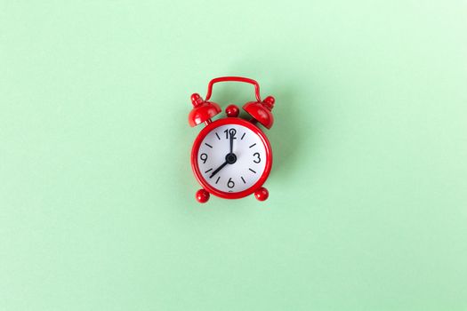Red small alarm clock on pastel green background with copy space, top view. Minimal retro style. Time management concept. Horizontal.