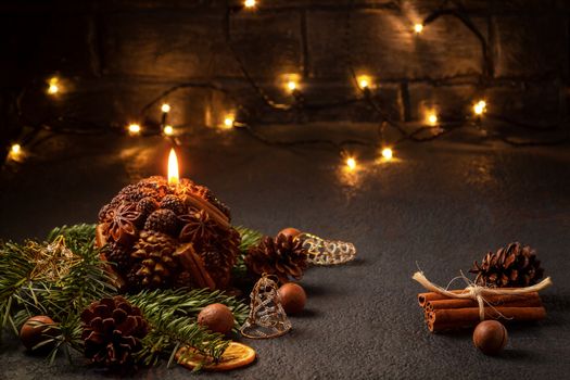 Christmas composition - decorative candle, Christmas tree branches and decorations on a dark background with blurry lights.