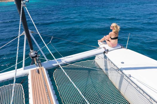 Woman in bikini tanning and relaxing on a summer sailin cruise, sitting on a luxury catamaran near picture perfect white sandy beach on Spargi island in Maddalena Archipelago, Sardinia, Italy.