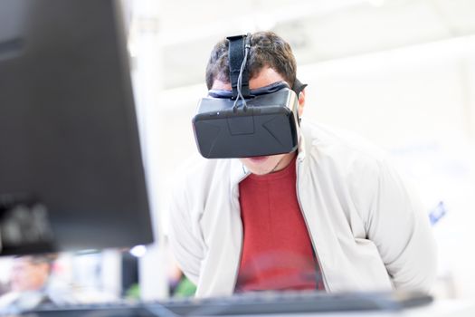 Young man wearing virtual reality headset and gesturing while sitting at his desk in creative office. Virtual reality in video games.