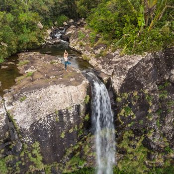 Active sporty woman relaxing in nature, practicing yoga on high clif by 500 feet waterfall at Black river gorges national park on tropical paradise island of Mauritius.