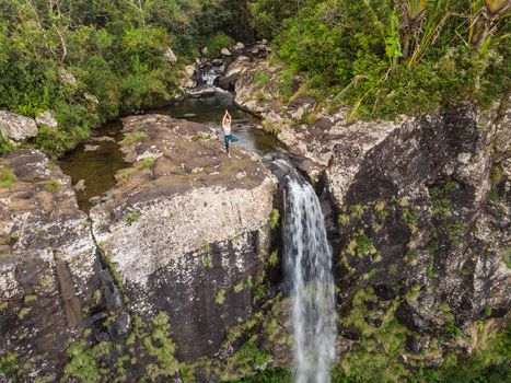 Active sporty woman relaxing in nature, practicing yoga on high clif by 500 feet waterfall at Black river gorges national park on tropical paradise island of Mauritius.