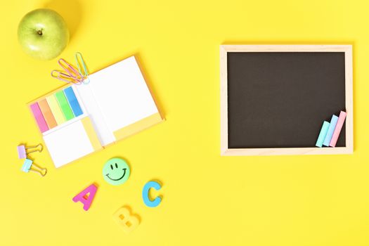 Chalkboard with wooden frame and colorful chalks and school stationeries, isolated on yellow background.