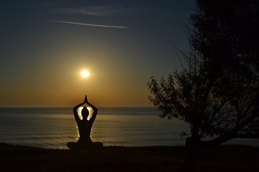 Silhouette of young woman practicing yoga on the beach at sunrise