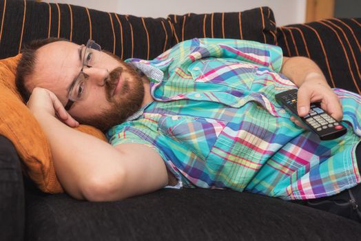 Man relaxing in sofa with remote control watching tv.