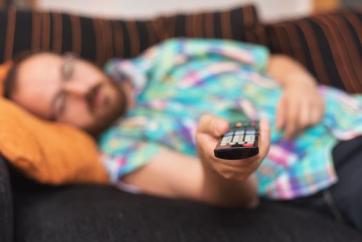Man relaxing in sofa with remote control watching tv. Shallow dof focus on remote control.